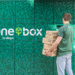 Zdjęcie zielonych paczkomatów one box. Przed nimi stoi kurier z paczkami.