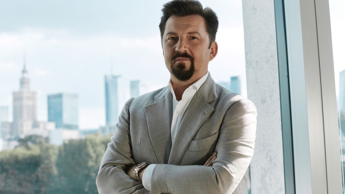 Dariusz Miłek, prezes zarządu Grupy CCC. Mężczyzna o ciemnym zaroście oraz szatynowych włosach. Ubrany w jasną marynarkę. W tle znajduje się panorama Warszawy