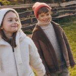 Resrved wadliwe produkty dla dzieci - sieć apeluje o zwrot. Na zdjęciu kampania Reserved Kids. Dziewczynka w jasnej bluzie z kapturem trzyma za rękę uśmiechniętego chłopca w pomarańczowej czapce, beżowym golfie i brązowej kurtce.
