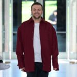 Sabato de Sarno odchodzi ze stanowiska dyrektora kreatywnego Gucci. Mężczyzna w długiej bordowej koszuli i białym T-shircie idzie po wybiegu, uśmiechając się do publiczności w tle. Ma krótkie ciemne włosy i kilkudniowy zarost.