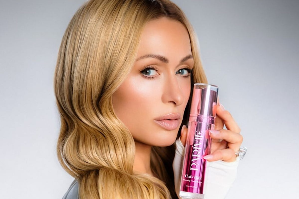 Paris Hilton reklamująca swoją nową markę kosmetyków skincare - Parívie, trzymająca w dłoni buteleczkę z produktem.